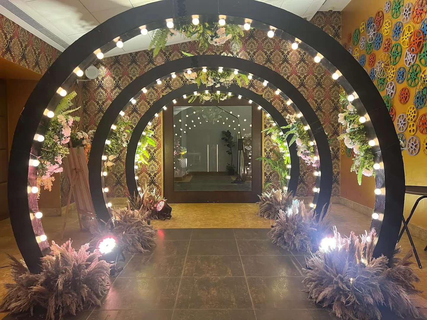Triple round arches lit with golden bulbs, pampas grass and florals